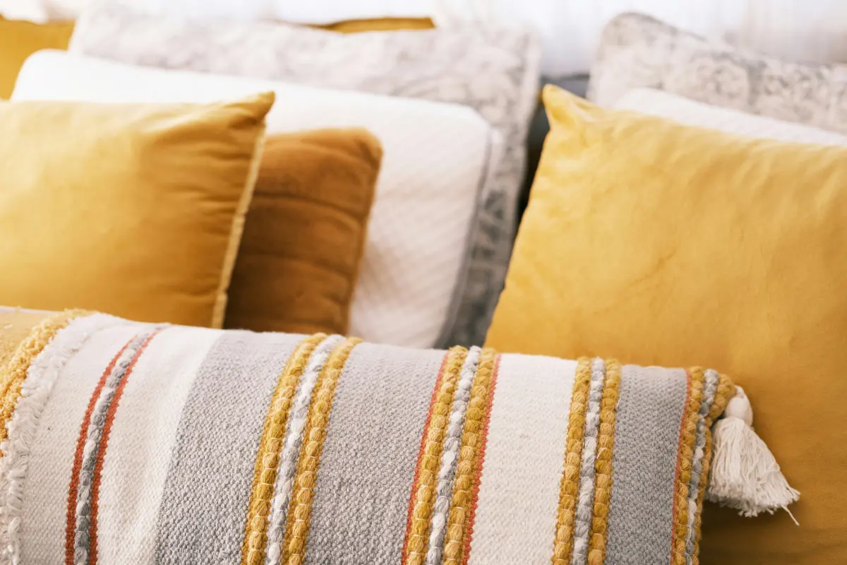 Boho style throw pillows on bed including yellow velvet pillow and gray-white-yellow striped long pillow with tassels