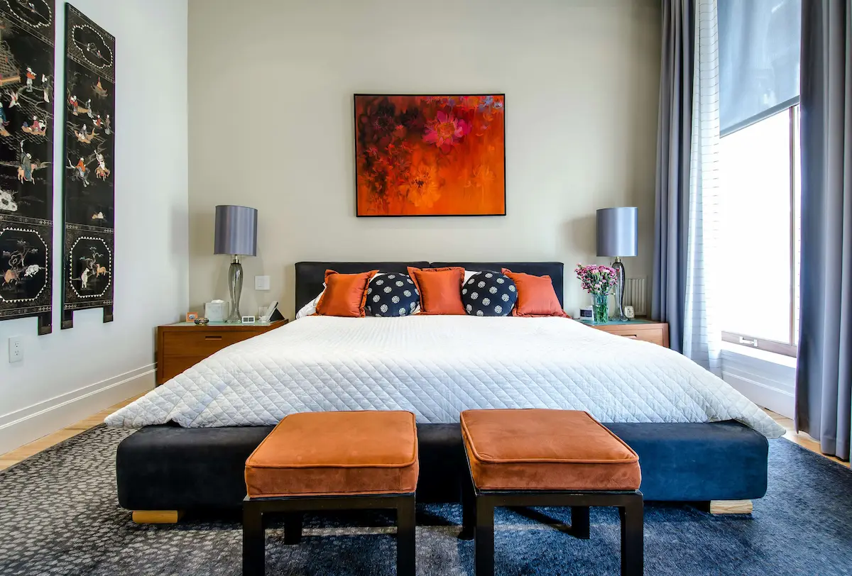 Modern spacious bedroom with large bed featuring white bedding and orange accent pillows