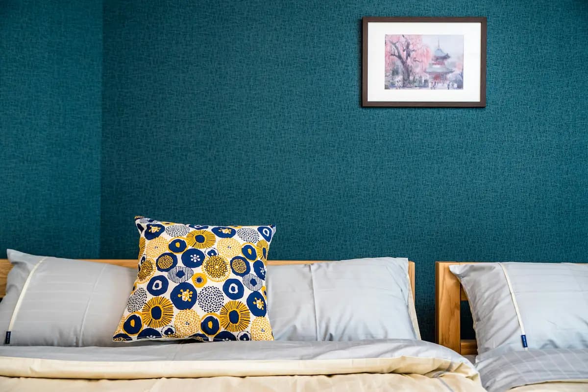 Bedroom with teal textured wall, bed with yellow-blue circular patterned accent pillow