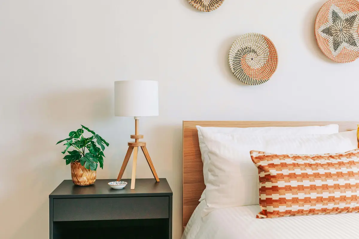 Modern bedroom nightstand with wooden tripod lamp and green plant