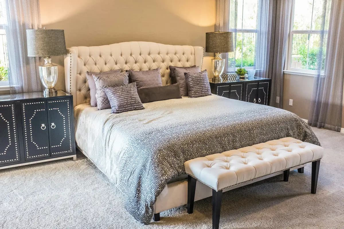 Luxurious bedroom with beige tufted headboard, gray-toned bedding and pillows, and black nightstands with stud detailing